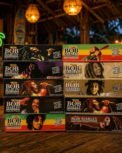 Ten packs of Bob Marley pure hemp king size rolling papers stacked in two columns on a wooden bar top, each pack carrying different artwork