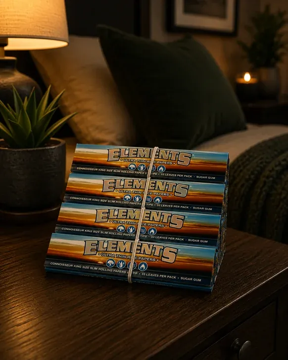Four packs of Elements Connoisseur king size slim rolling papers with tips, tied with twine on a dark wood nightstand beside a lamp