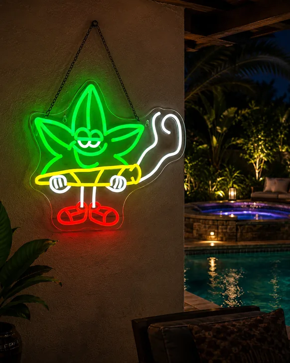 A neon sign of a cartoon leaf character in green, yellow and red, lit and hanging by a chain on a stucco wall beside a lit pool at night