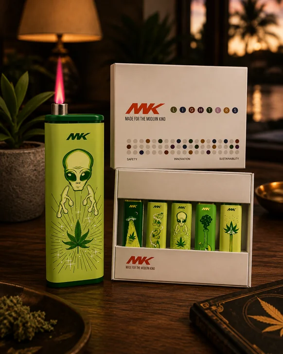 A green MK lighter printed with an alien and a cannabis leaf burning with a pink jet flame, standing beside its open box of five more printed lighters on a dark wood table