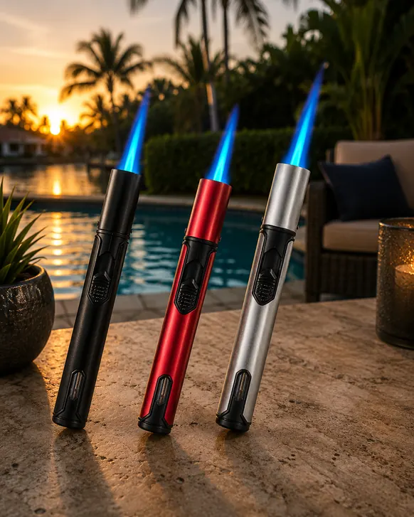 Three refillable pen torches standing on a travertine pool deck at sunset, in black, red and silver, each lit with a blue jet flame and showing a fuel window near the base